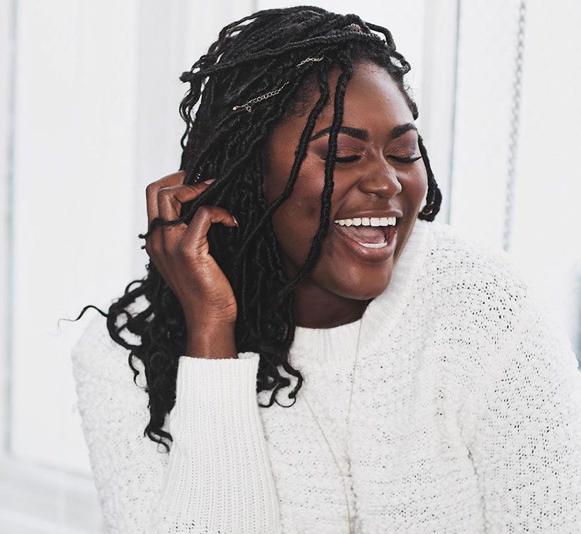 Danielle Brooks laughing and wearing a white jumper as she holds her hand to her face 