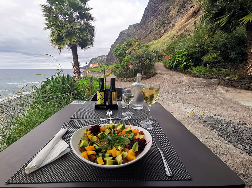 Enjoying a vegan quinoa salad with fresh fruit, including mango and avocado with a sea view at Faja Dos Padres restaurant in Madeira