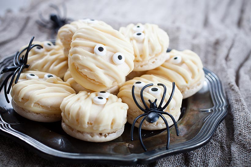 A plate of macarons decorated to look like mummies for Halloween - vegan Halloween recipes