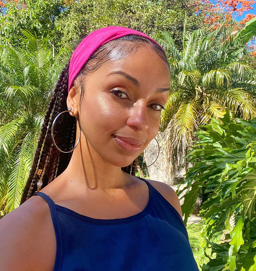 Musician Mýa wearing a fuscia pink headscarf and hoop earrings on a sunny day outdoors 