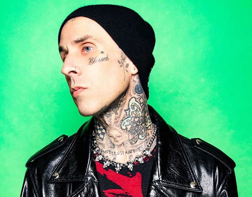 Vegan celebrities - Travis Barker wearing a black beanie and a leather jacket with tattoos on his face and neck 