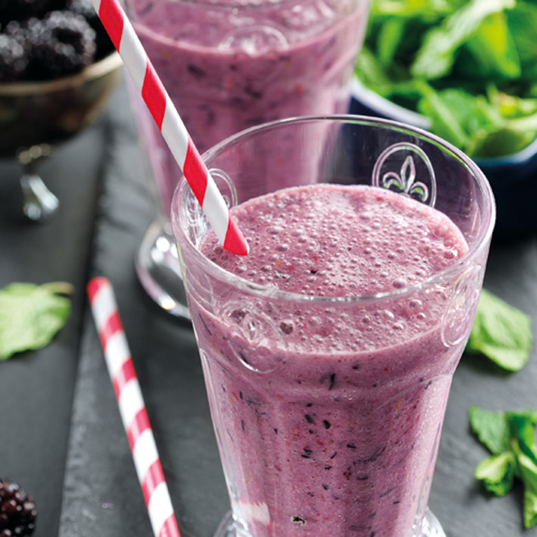 Triple berry smoothie in a glass with red and white striped straw